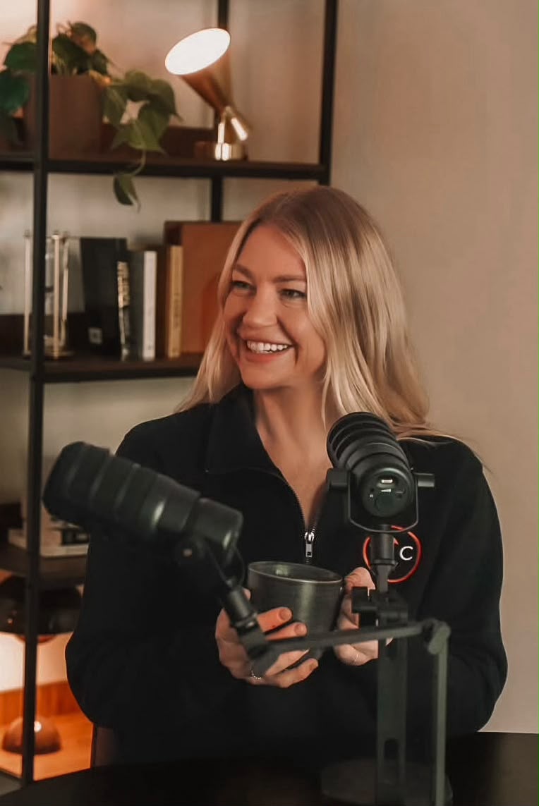 Bianca Criaco laughing in the studio, holding a mug between two microphones